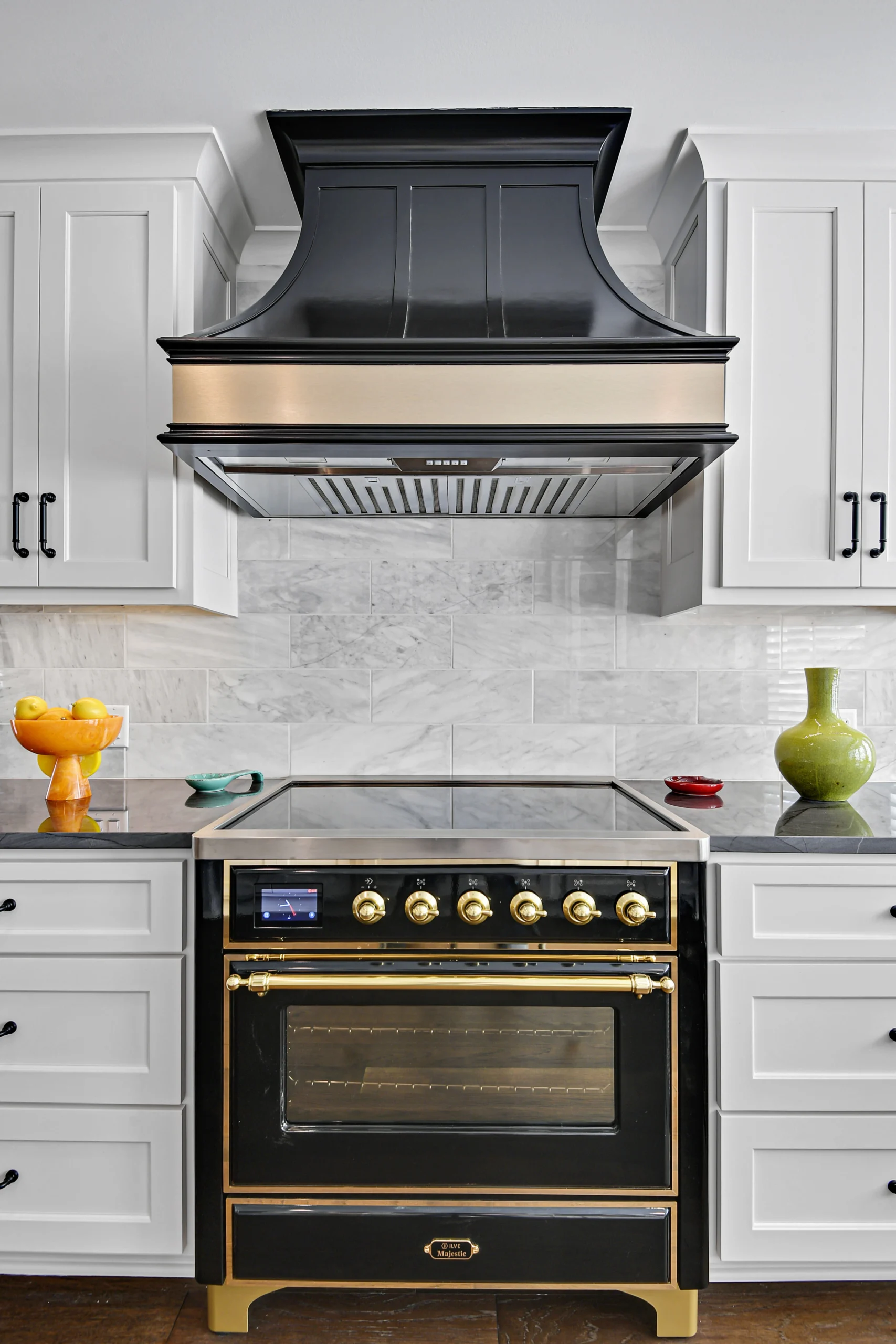 High-end kitchen remodelling with a custom black range hood, marble backsplash, and modern white cabinets